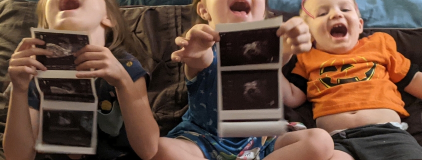 children holding ultrasound pictures and laughing