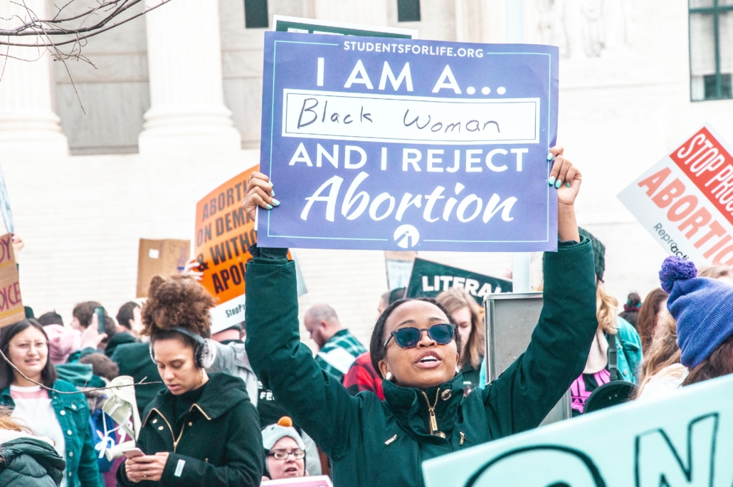 A Black woman raises a pro-life sign above her head