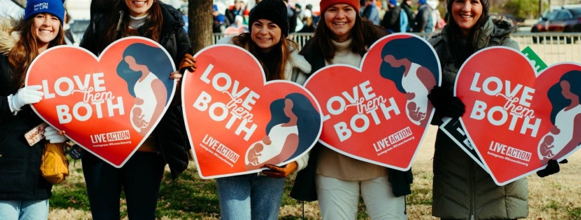 Young women holding "Love Them Both" signs