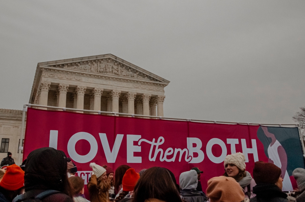 Young people stand with a "Love Them Both" banner in front of the Supreme Court