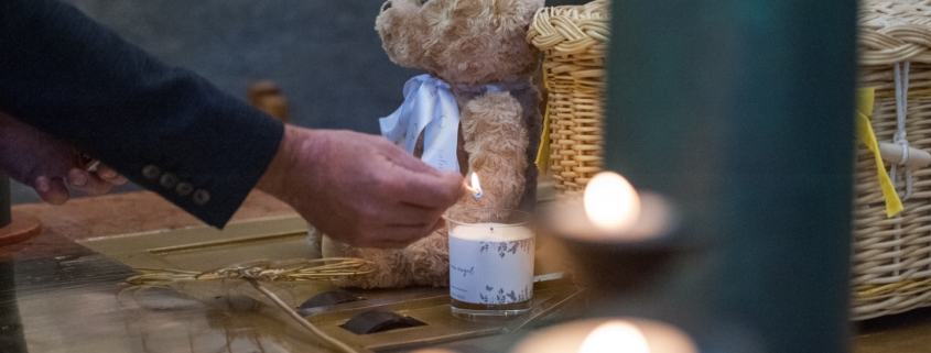 A person lights a candle near a child's teddy bear